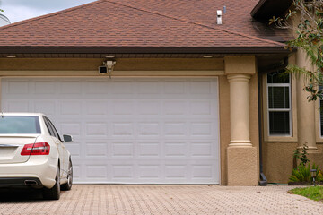 Vehicle parked in front of wide garage double door on paved driveway of typical contemporary...