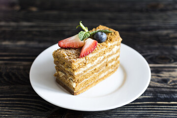 A cake with white cream and a decor of red and blue berries in close-up on a white plate.