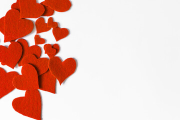 An abstract background of a scattering of bright red fabric hearts on a white background is a place for text.