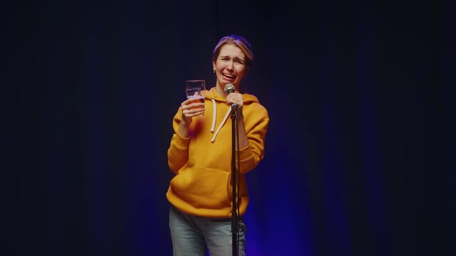 Drunk woman crying on stage, drinking beer and saying toast. Female comedian speaking with audience, saying toast, public monologue. 