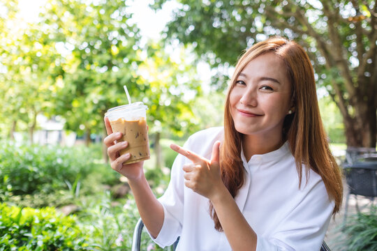 Portrait image a young asian woman holding and pointing finger at a cup of iced coffee in the outdoors
