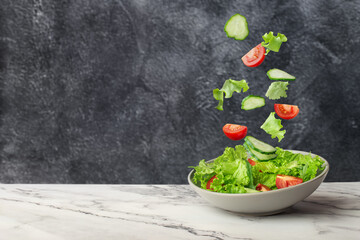 salad of fresh green vegetables falling into a plate on a gray background