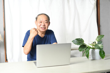 パソコンの前でガッツポーズする高齢者男性