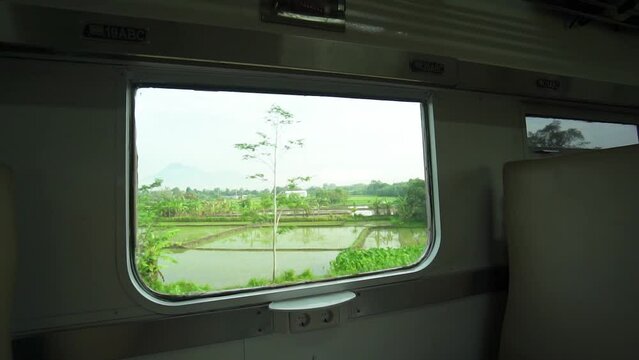 Ride the train sitting by the window looking at the view of the tracks and rice fields outside the window the train is speeding towards its destination