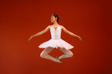 Fototapeta na wymiar Beautiful Asian woman ballet dancer practice dance jump move wearing tutu at home red orange background wall