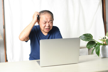 ノートパソコンの前で悩む高齢者男性