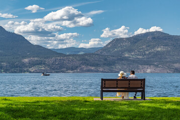 Rear view of a romantic young couple sitting on the bench enjoying the view of a beautiful lake.