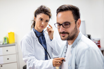 Young female doctor listen to male patient heart chest with stethoscope at clinic meeting. Woman GP...