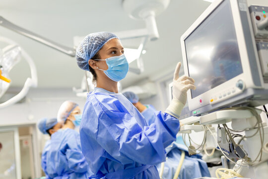 Portrait of a young female doctor in scrubs and a protective face mask preparing an anesthesia machine before an operation