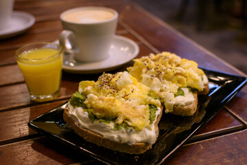 Momento saludable. Tostadas aderezadas con huevo y aguacate. Café con jugo de naranjas desenfocados en el fondo.
