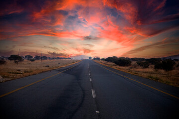 Fototapeta na wymiar Beautiful South African road that runs through the middle of the African savannah under the typical African sun, which is characterized by beautiful colors at sunset.