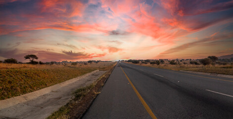 Travel on a road that runs through the middle of the African savannah of South Africa at sunset, it is a beautiful road with a beautiful sky with typical colors of the African sun.