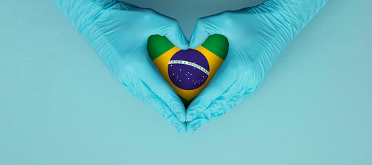Doctors hands wearing blue surgical gloves making hear shape symbol with brazil flag