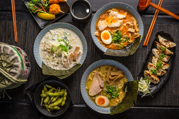 Ramen combo platter with Pork tonkotsu chashu ramen, soy ramen, crab claw, edamame soybeans, spicy fried pork gyoza dumplings on black table, Top view