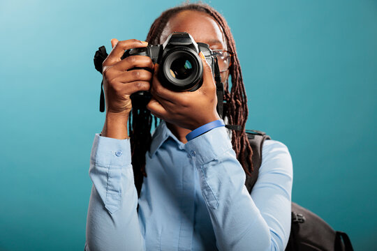 African american young adult photography entusiast with modern photographing device taking photos on blue background. Confident and creative photographer taking pictures while enjoying leisure time.
