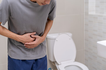 man standing has diarrhea and severely toxic food. Man touch belly in the bathroom. Abdominal pain, Diarrhea, Colon cancer concept