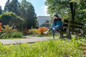 Naklejka na ściany i meble woman sitting on the bench at city public park reading electronic book