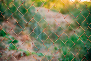 Mesh cage in the garden with green grass as background. Metal fence with wire mesh. Blurred view of the countryside. Abstract background.