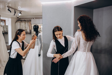 Female making adjustment to wedding gown in fashion designer studio. Bride wearing her wedding gown...