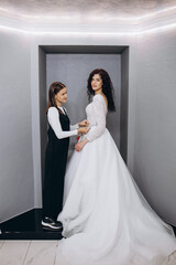 Naklejka premium Bride at the clothes shop for wedding dresses; she is choosing a dress and the designer are assisting her
