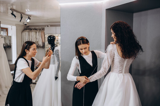 Female making adjustment to wedding gown in fashion designer studio. Bride wearing her wedding gown with female dress designer making final adjustments on dress.