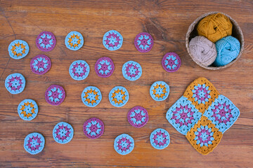 Layout of small crochet patterns, motif of multicolored squares and a basket with cotton skeins on vintage wooden surface.