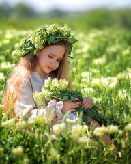 Portrait of a cute village girl kid in a wreath on a flower field.. A child in a blooming meadow.