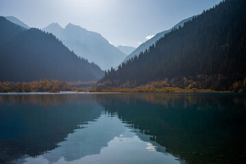 Serenity lake in the mountains. Foggy autumn morning with mountains and reflection.