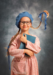 Close portrait of a happy girl kid with two flying braids on a gray background with book
