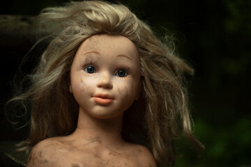 Doll's head is in mud. Children's toy. Dirty rubber girl's head with hair.