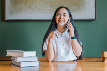 Smiling young Asian woman talking on the phone and working at home.