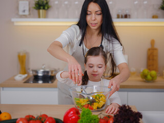 Happy mother and daughter enjoy prepare freshly salad together in kitchen. Healthy food at home. Healthy Lifestyle and Eating Concept. little influencer filming blog about healthy eating