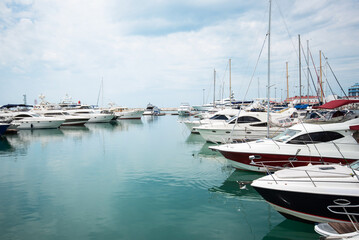 Obraz premium Luxury yachts docked in sea port. Marine parking of modern motor boats and azure water. Tranquility, relaxation and fashionable vacation. White yachts and sailboats moored in marina, summer season.