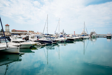 Fototapeta premium Luxury yachts docked in sea port. Marine parking of modern motor boats and azure water. Tranquility, relaxation and fashionable vacation. White yachts and sailboats moored in marina, summer season.