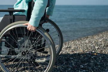 Fototapeta na wymiar Caucasian woman in a wheelchair on the seashore. Close-up of female hands.