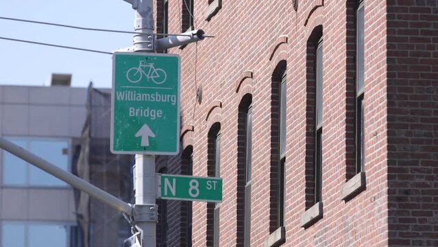 North 8th Street Sign in Williamsburg, Brooklyn, and an arrow pointing to the Williamsburg Bridge. Red brick building in the background.