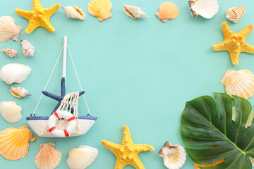 nautical concept with sail boat, star fish and seashells over mint blue wooden background