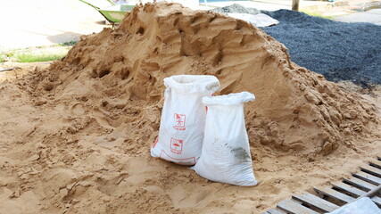 White sandbags and piles of sand. Close-up of old plastic sacks reused to contain sand for...