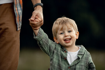 dad holds the hand of a happy kid, a little boy smiles. Father and child are walking together. Family leisure, holidays with children. Fatherhood, upbringing. Father's Day. Friendly family concept