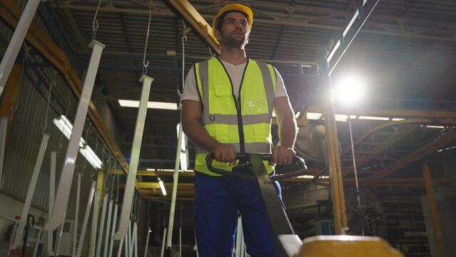 Young metalworker man in a industrial factory pushing load cart to transport pallets