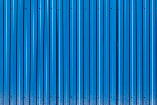 Fence made of blue profiled sheeting with mud splashes in the lower part