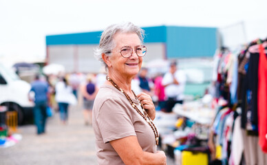 Senior woman at the flea market looking for second hand  clothes, shoes, bags, jewellery. Zero...