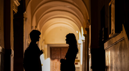 Silhouette of two young people chatting on school building corridor with sunlight and shadow