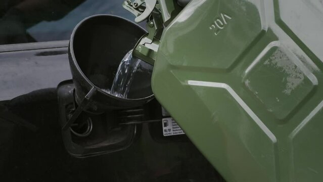 Man pours gasoline from a green canister directly into the tank of a car. Green Jerrycan full of gas. Lack of fuel while traveling far. Close-up footage of gasoline flow in a slow motion