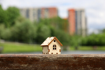 Obraz na płótnie Canvas Wooden house model on background of summer lake and high-rise residential buildings. Concept of country cottage, real estate in ecologically clean area