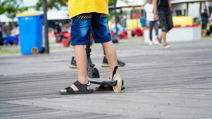 Fototapeta premium Person on roller skates. Child playing scooter outdoors. Small child's feet and scooter.