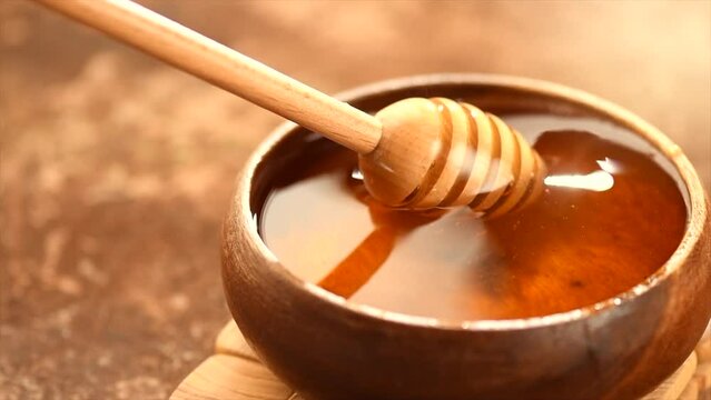 Honey dripping, pouring from honey dipper in wooden bowl.  Close-up. Healthy organic fresh thick honey dipping from the wooden honey spoon, closeup. 4K UHD video footage. Slow motion. 