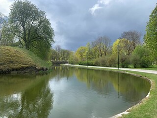 Beautiful park with green trees just before the rain. The water of the river is still. 
It is...