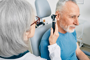 Otolaryngologist doctor checking senior man's ear using otoscope or auriscope at hearing center....