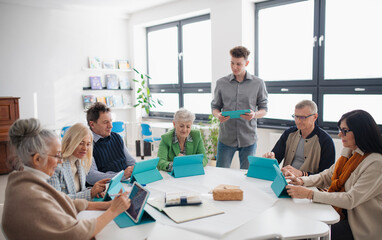 Group of seniors attending IT class in community centre with teacher